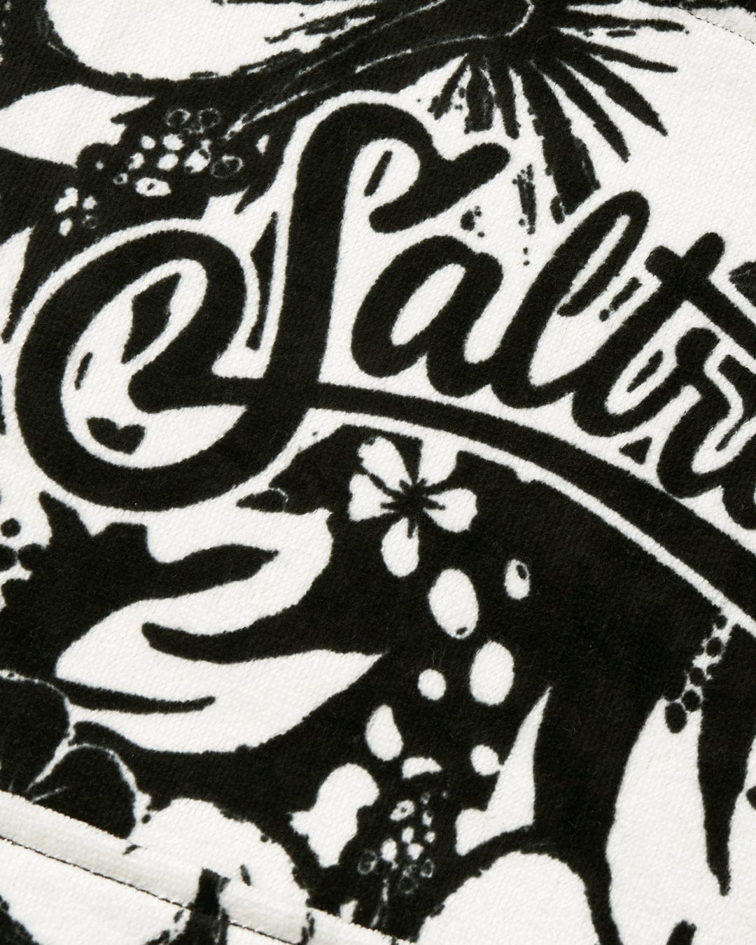 Close-up of a black and white 100% cotton Hibiscus - Kids Changing Towel by Saltrock with a floral design and the word "saltwater" scripted across it.