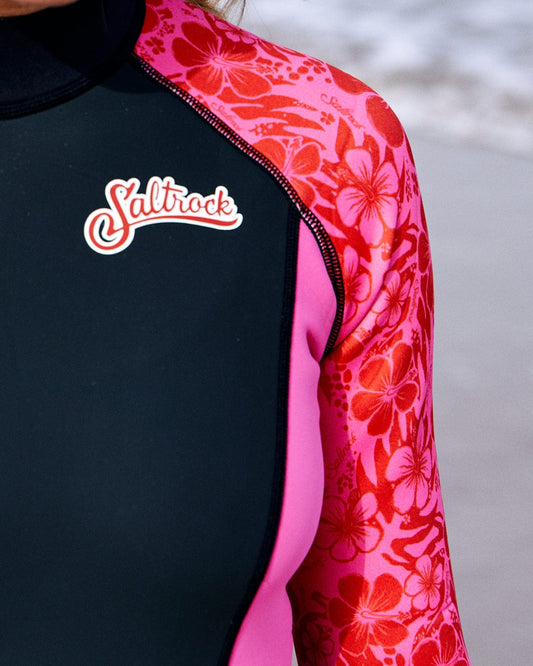 Close-up of a person wearing a black and pink Hibiscus - Womens Full Wetsuit - Pink neoprene wetsuit with the Saltrock logo on the chest.