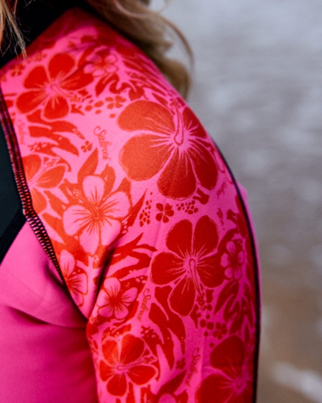 Close-up view of a person wearing a bright pink neoprene wetsuit with a Saltrock - Womens Full Wetsuit - Pink on the sleeve.