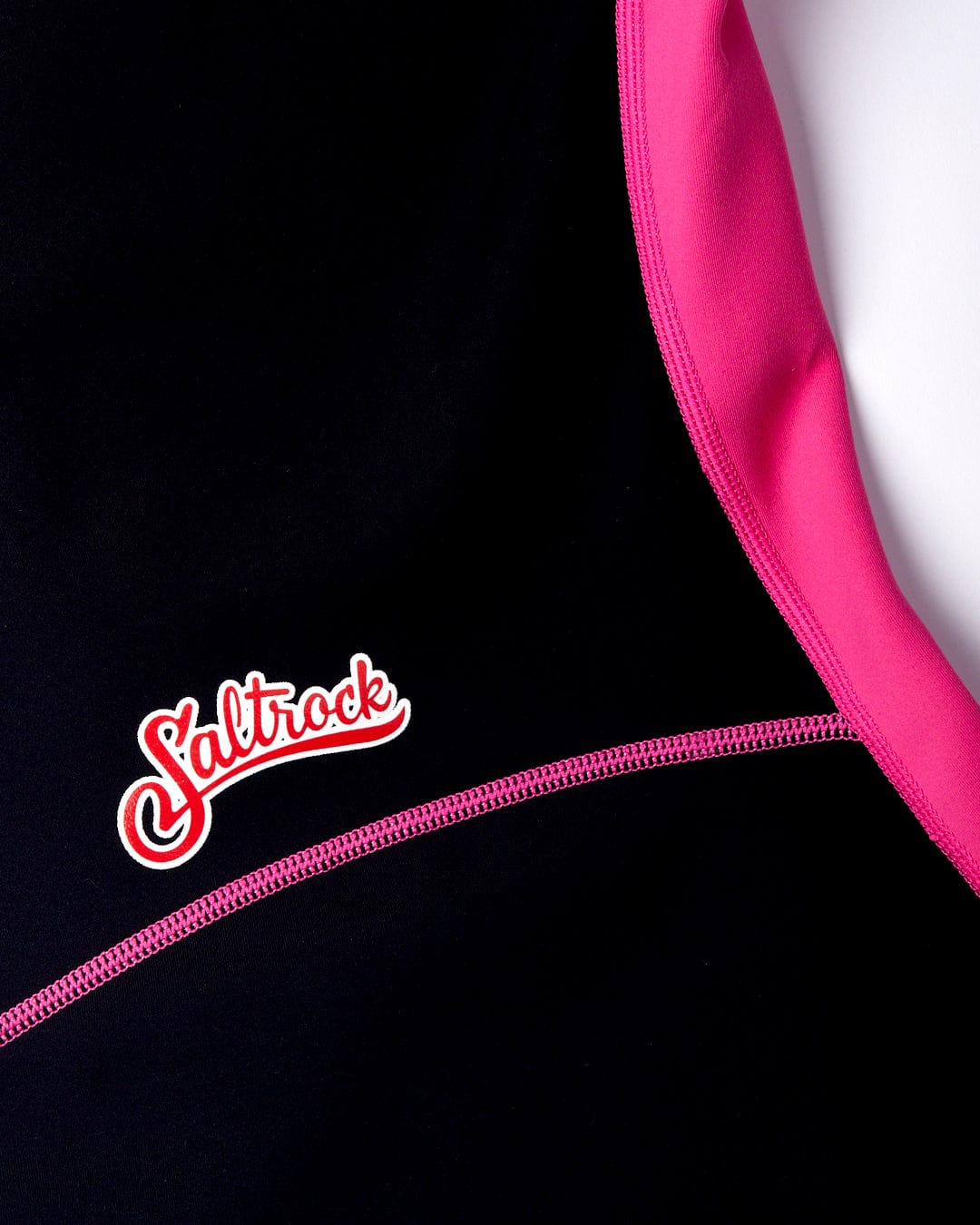 Close-up of a Saltrock logo on a black and pink neoprene wetsuit with visible seam and zipper detail featuring the Hibiscus - Womens Springsuit - Pink.