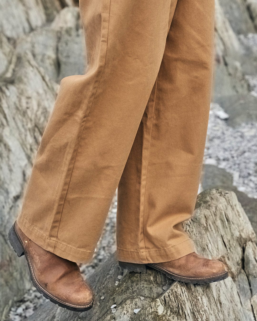A person experiencing comfort while standing on rocks wearing a pair of tan Saltrock Hilda Twill - Womens Trousers - Light Brown.