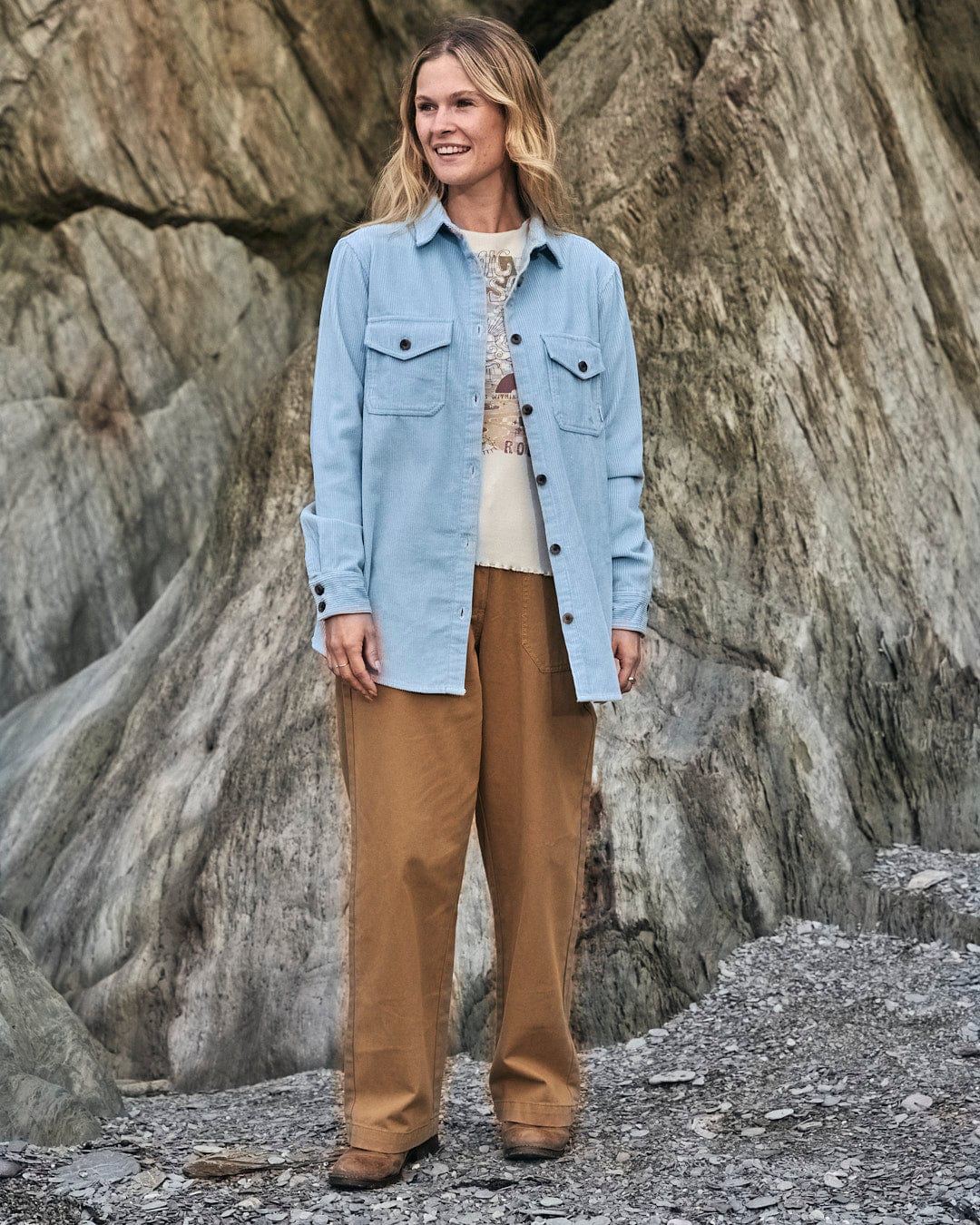 A woman wearing Saltrock's Hilda Twill - Womens Trouser - Light Brown standing in front of rocks.