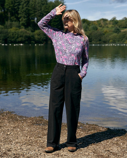 A woman is standing on the shore of a lake wearing Hilda Twill - Womens Trouser in Black by Saltrock.