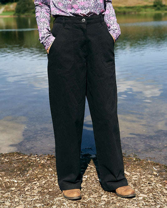 A woman in Saltrock's Hilda Twill - Womens Trouser - Black standing next to a body of water.
