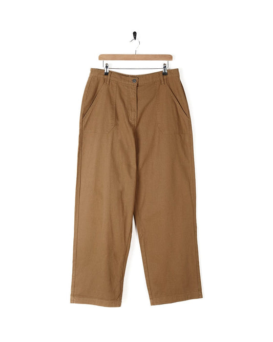 A pair of Hilda Twill - Womens Trouser - Light Brown trousers hanging on a hanger, made by Saltrock.