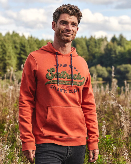 A man in a red Home Run Chenille - Mens Pop Hoodie by Saltrock standing in a field.