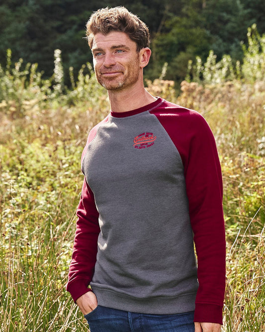 A man wearing a Saltrock Home Run - Mens Long Sleeve Sweat - Grey/Red with contrasting red sleeves in a field.