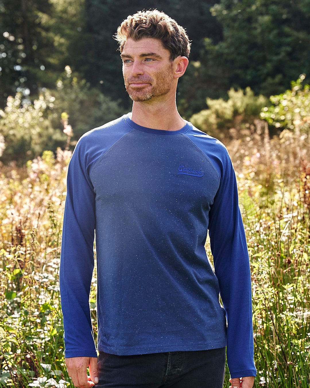 A man wearing a blue long sleeve t-shirt with Saltrock branding standing in a field.