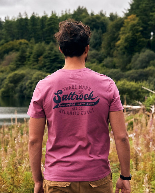 A man wearing a Saltrock Home Run - Mens Short Sleeve T-Shirt - Dark Pink looking at a lake.