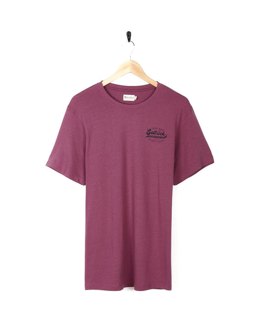 A Saltrock Home Run - Mens Short Sleeve T-Shirt - Dark Pink hanging on a wooden hanger.