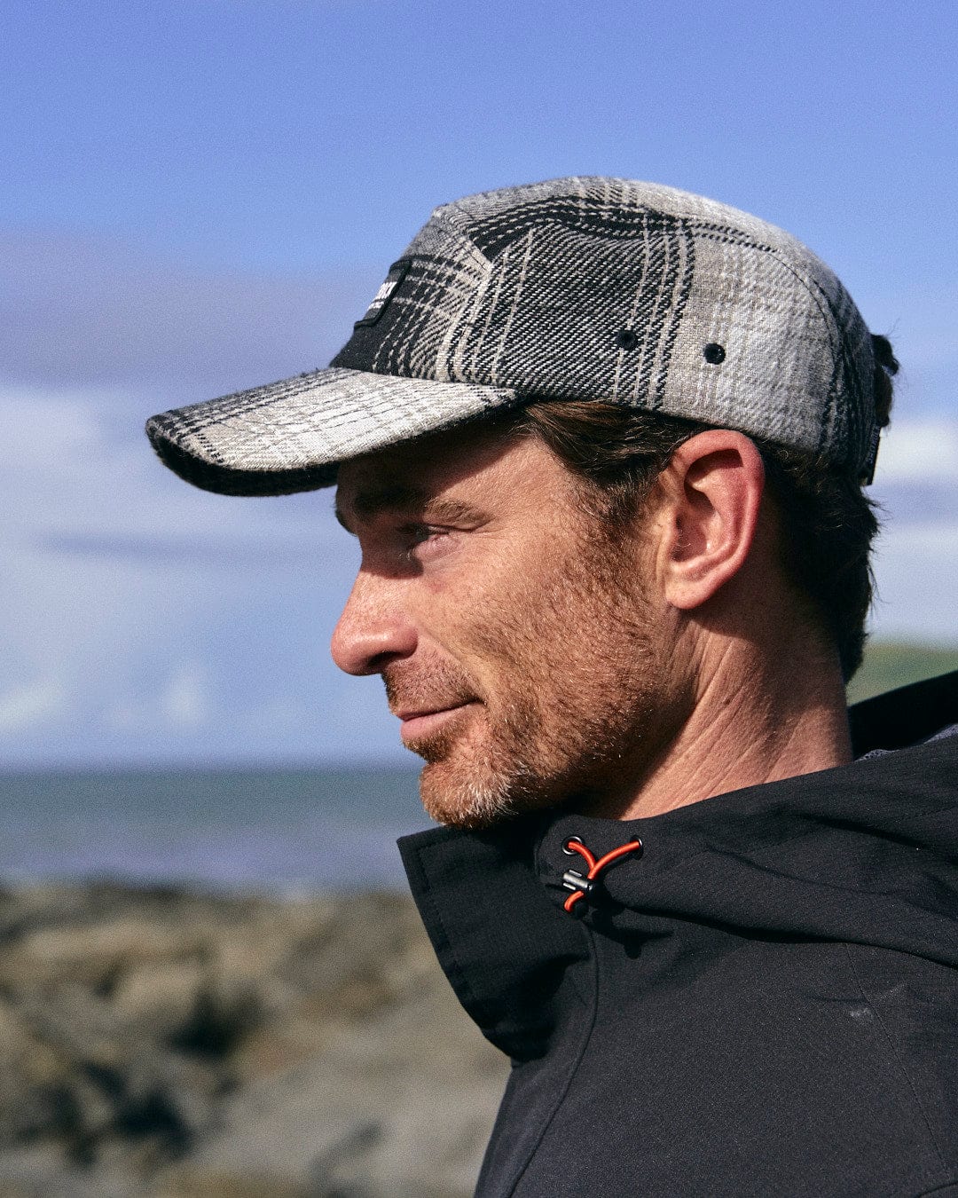 A man wearing a Saltrock Hunter - 5 Panel Cap - Grey, looking at the ocean.