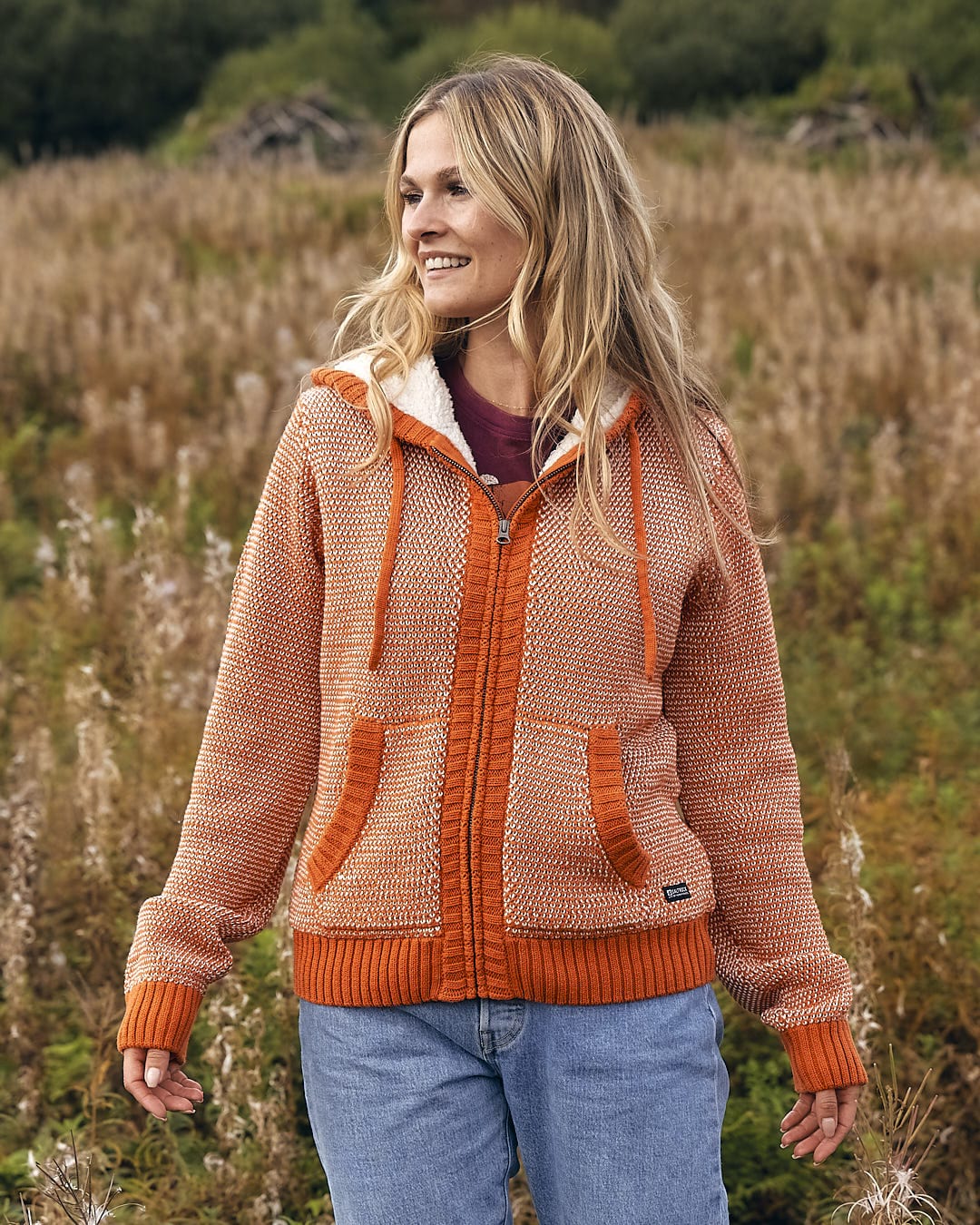 A woman is standing in a field wearing a Saltrock - Helly Womens Borg Lined Knitted Hoodie - Orange.