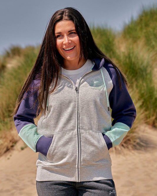 A woman wearing a Saltrock Jan Womens Zip Hoodie - Grey on a beach, exuding effortless style.