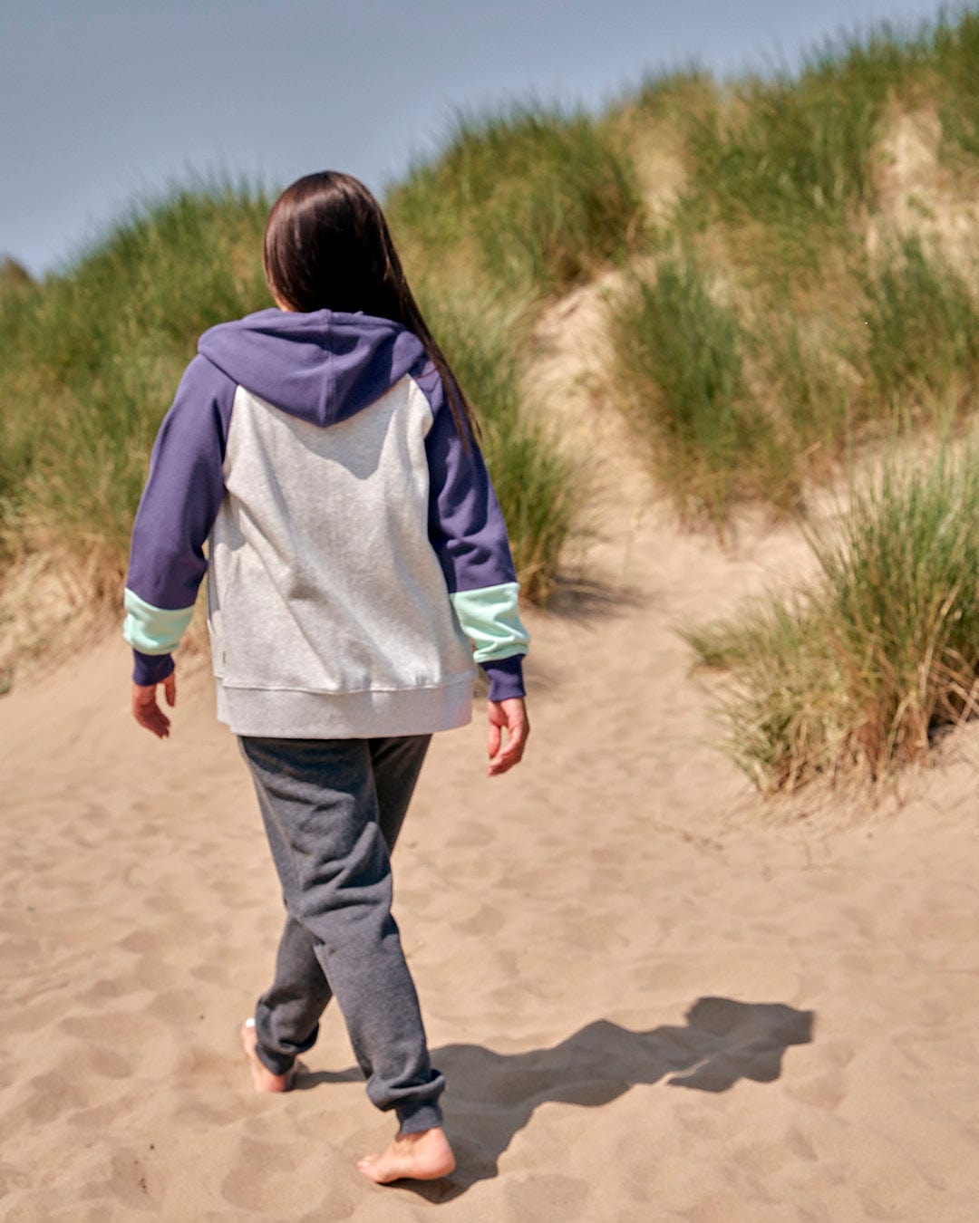 A girl walking on a sand dune wearing a Saltrock Womens Zip Hoodie - Grey and sweatpants.