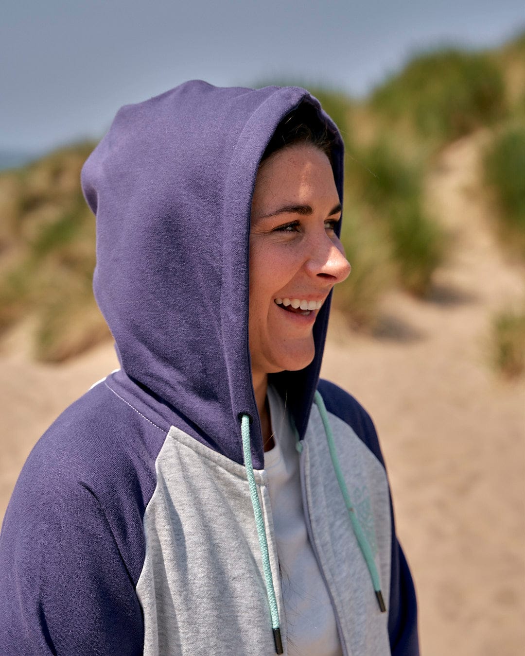 A woman wearing a Saltrock Jan Womens Zip Hoodie - Grey on a beach, showcasing effortless style with Saltrock branding.