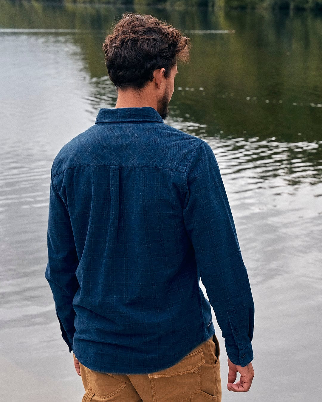 A man is standing by a lake in a Saltrock Jaxon - Mens Check Long Sleeve Shirt - Dark Blue.