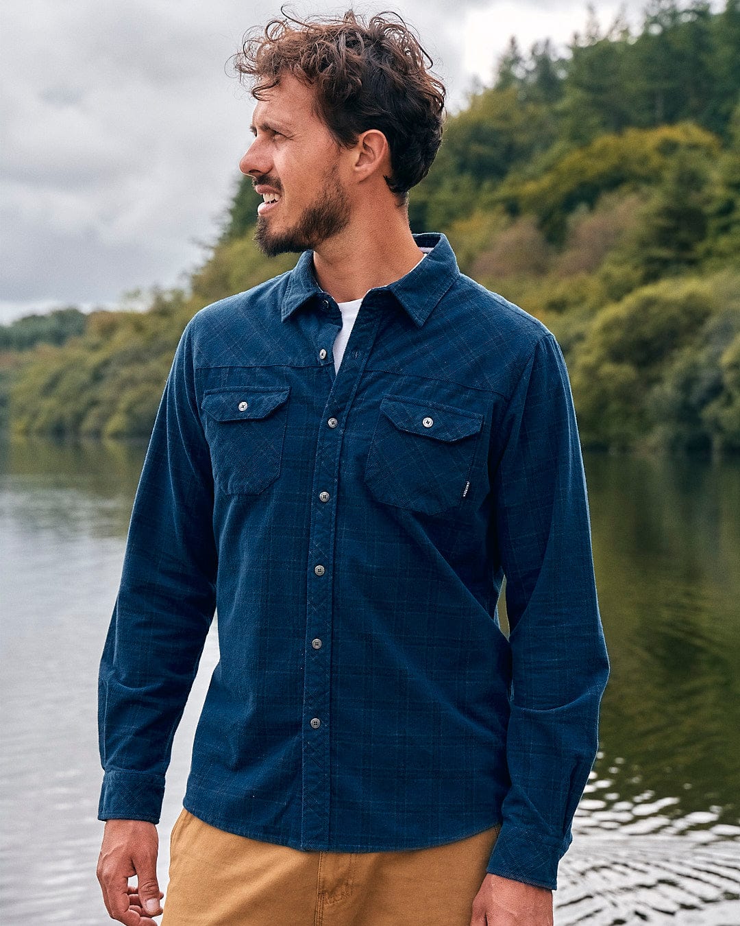 A man standing by a lake wearing a Jaxon - Mens Check Long Sleeve Shirt - Dark Blue from Saltrock.