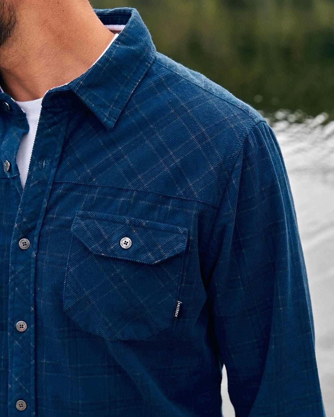 A man is standing next to a lake wearing a Saltrock Jaxon - Mens Check Long Sleeve Shirt - Dark Blue.