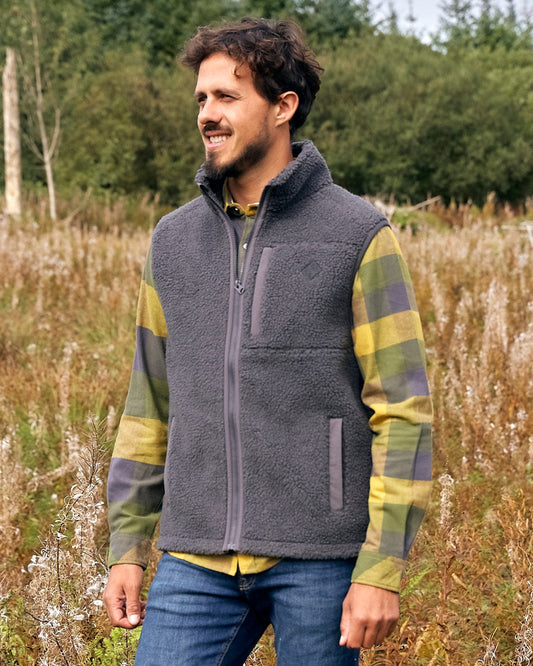 A man is standing in a field wearing a Saltrock Joel - Mens Sherpa Fleece Gilet - Dark Grey.