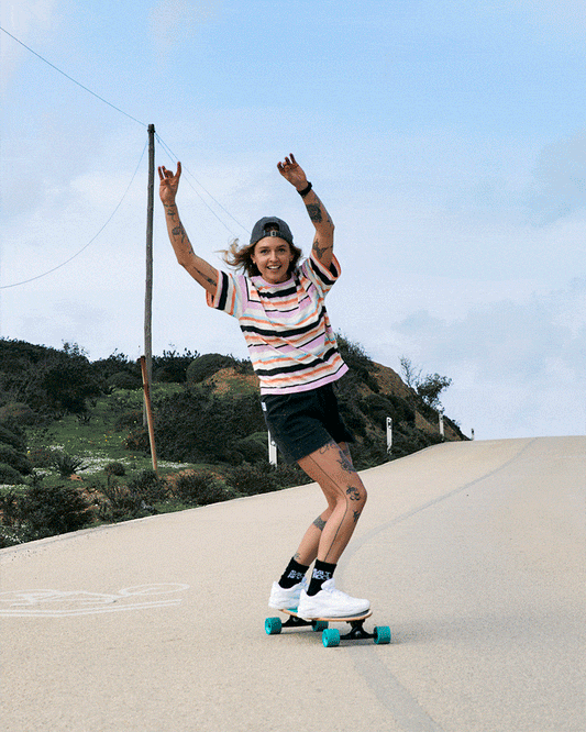 Woman joyfully skateboarding down a hill on a sunny day, raising her arms in excitement, wearing Saltrock's Juno - Womens Short Sleeve T-Shirt - Multi and shorts.