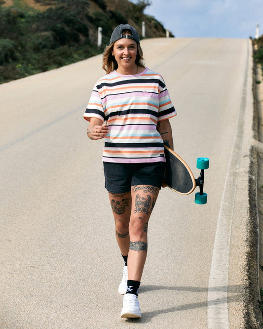 Woman with tattoos and an Saltrock Juno - Womens Short Sleeve T-Shirt in Multi stripe pattern, walking with a skateboard on a sunny day.