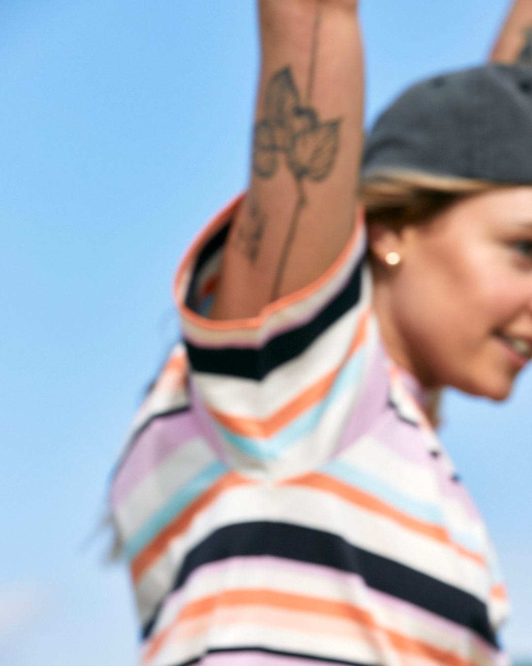 A blurred photo of a person raising their arm to reveal a tattoo, against a blue sky background with an embroidery design on the Saltrock Juno - Womens Short Sleeve T-Shirt - Multi.