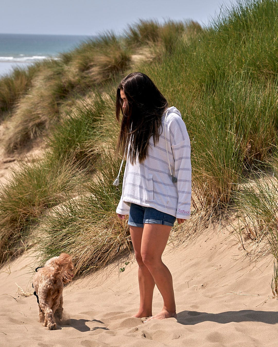 A woman is walking her dog on a beach wearing the Kennedy - Womens Pop Hoodie in Cream by Saltrock.