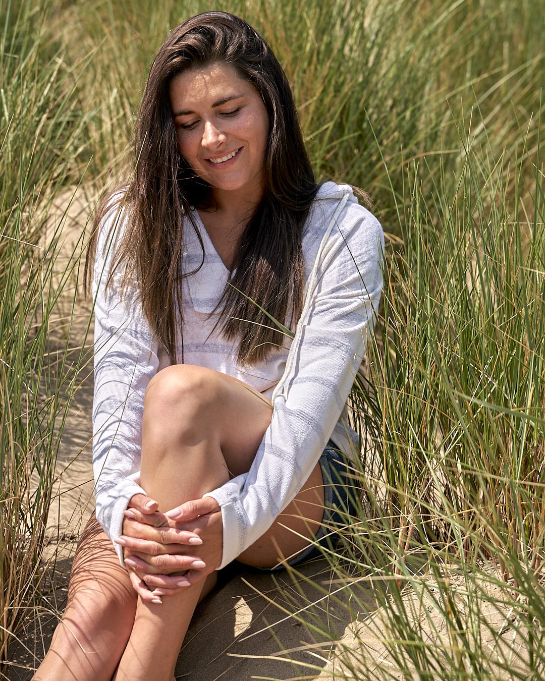 A woman sitting in the sand with a Saltrock Kennedy - Womens Pop Hoodie - Cream.