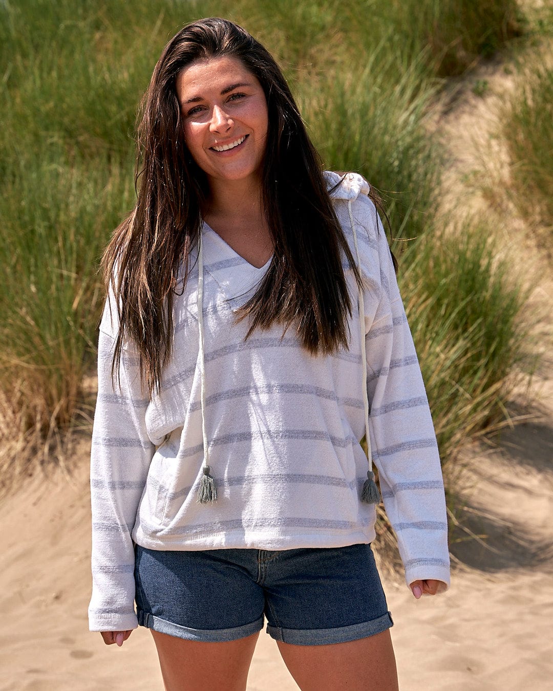 A young woman in shorts and a Saltrock Kennedy - Womens Pop Hoodie - Cream standing in the sand.