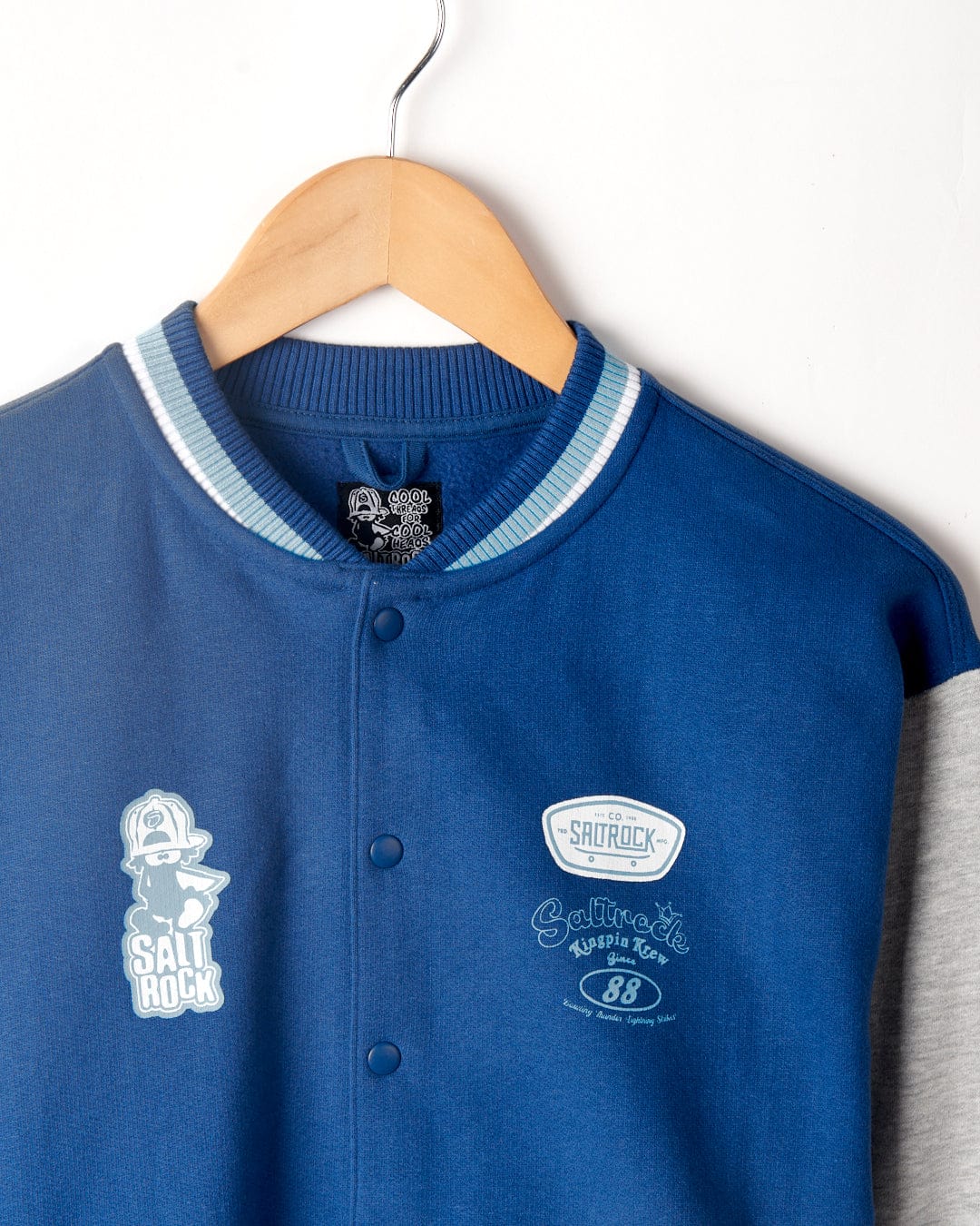 A Krew - Recycled Varsity Bomber Jacket - Blue on a hanger, featuring distinctive Saltrock branding and a "Cool & Sassy" tag, crafted from recycled material.