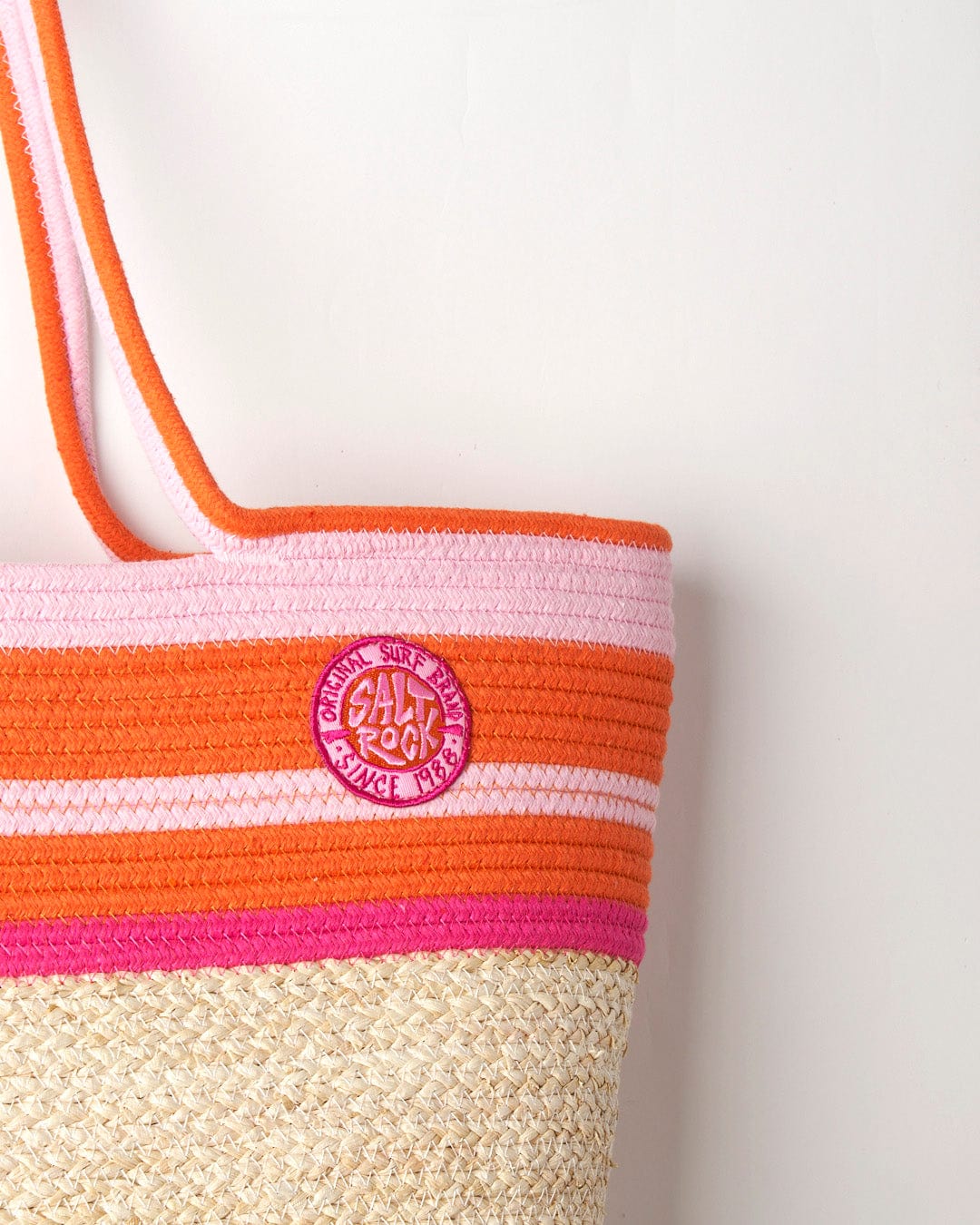 Striped Las Cora Straw Beach Bag - Cream with a pink logo patch on a white background and straw bottom by Saltrock.