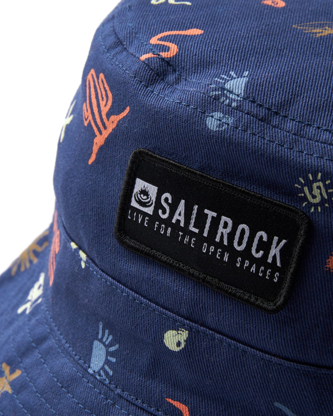 A close-up of a Last Stop - Bucket Hat - Blue adorned with a Saltrock nylon badge, featuring intricate dessert graphics and made from 100% cotton.