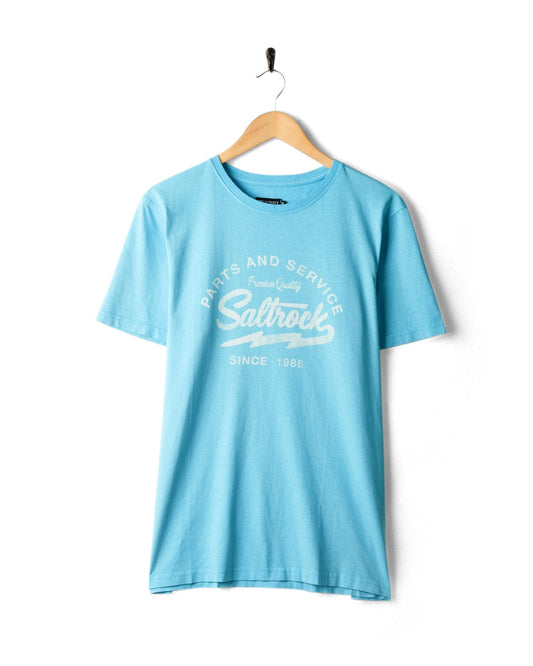 A Last Stop Motel - Mens T-Shirt - Light Blue with Saltrock branding hangs on a wall-mounted hook against a white background.