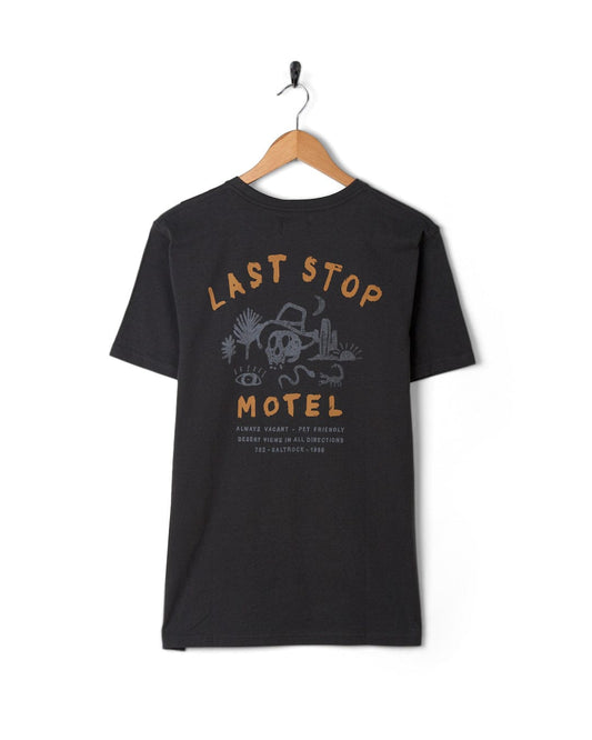 A Saltrock mens short sleeve t-shirt in dark grey with the "Last Stop Motel" design, hanging on a wall-mounted hook.