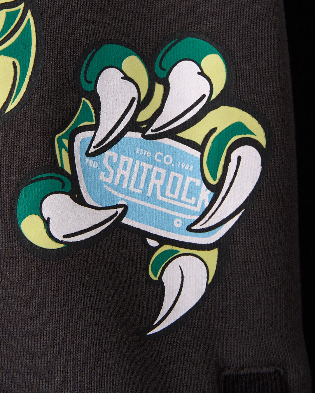 Graphic of a creature's claw holding a blue sign that reads "Saltrock" with the text "ESTD CO. 1988" in the background on a dark fabric. The glow-in-the-dark graphics add an eerie effect, perfect for an oversized fit made from recycled materials. Introducing the Saltrock Las Vegas Smackdown - Recycled Oversized Kids Zip Hoodie - Black.