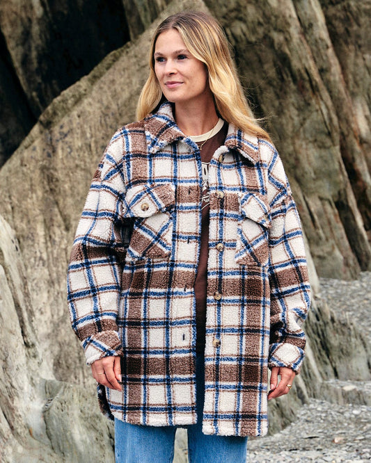 A woman wearing a Saltrock Laurie - Womens Check Sherpa Fleece Coat in Cream standing on a rock.