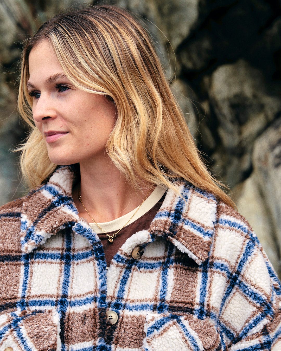A woman in a Saltrock Laurie - Womens Check Sherpa Fleece Coat - Cream standing in front of rocks.