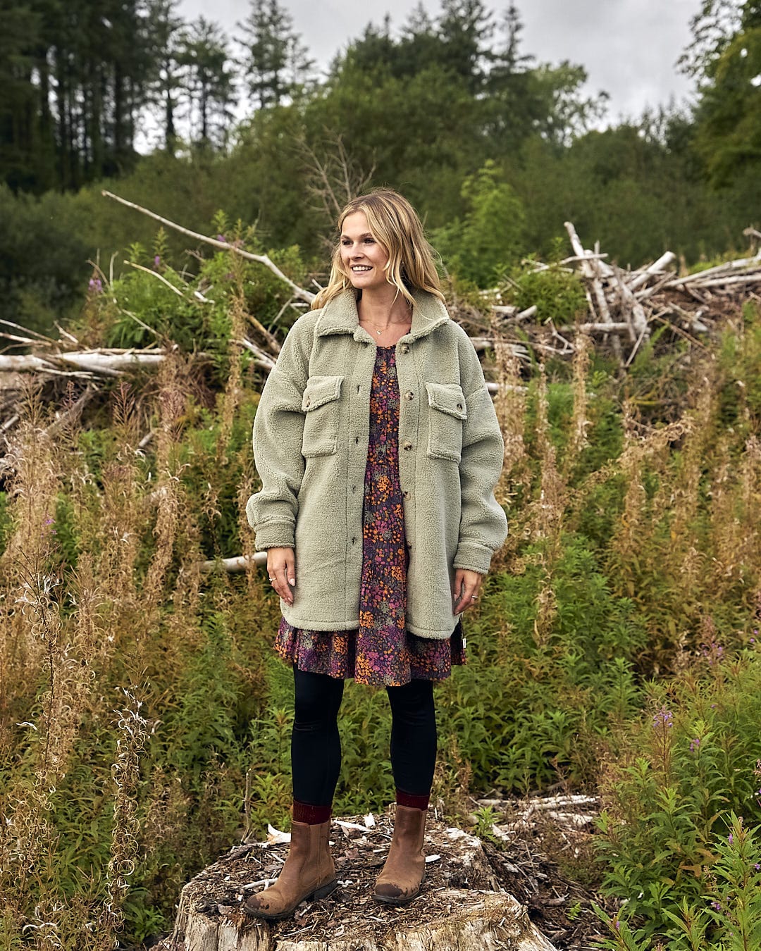 A woman standing on a log in a wooded area wearing the Laurie - Womens Sherpa Fleece Coat - Green by Saltrock.