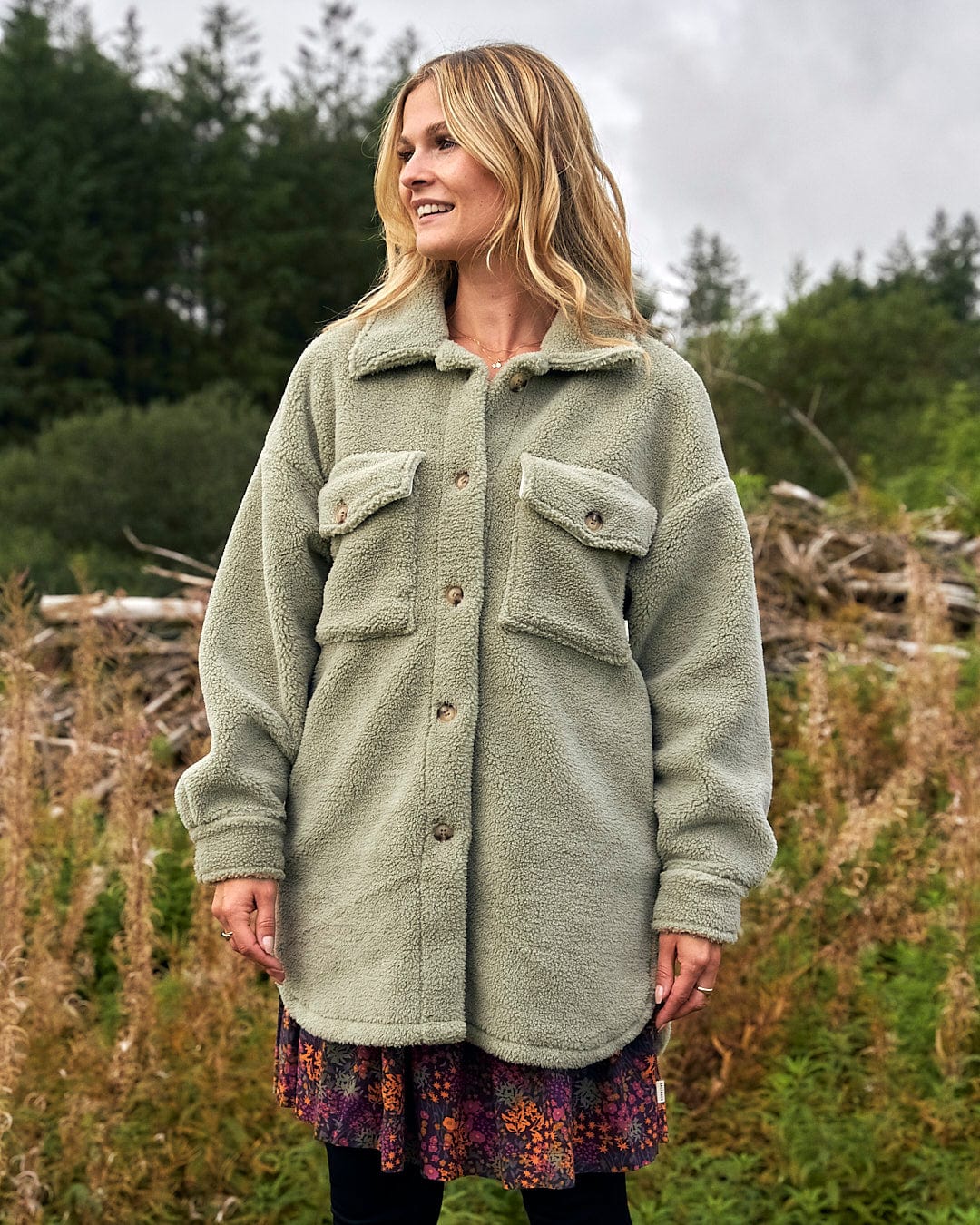 A woman is standing in a field wearing a Laurie - Womens Sherpa Fleece Coat - Green, from the brand Saltrock.