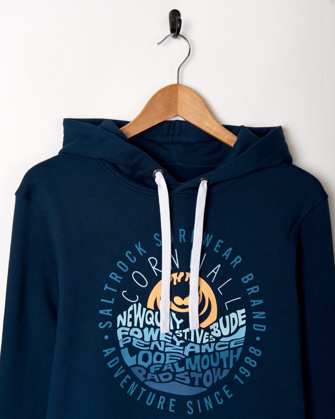 Navy blue cotton Layers Cornwall - Mens Pop Hoodie - Blue with white drawstrings hanging on a wall hook, featuring a chest print with text related to Cornwall by Saltrock.