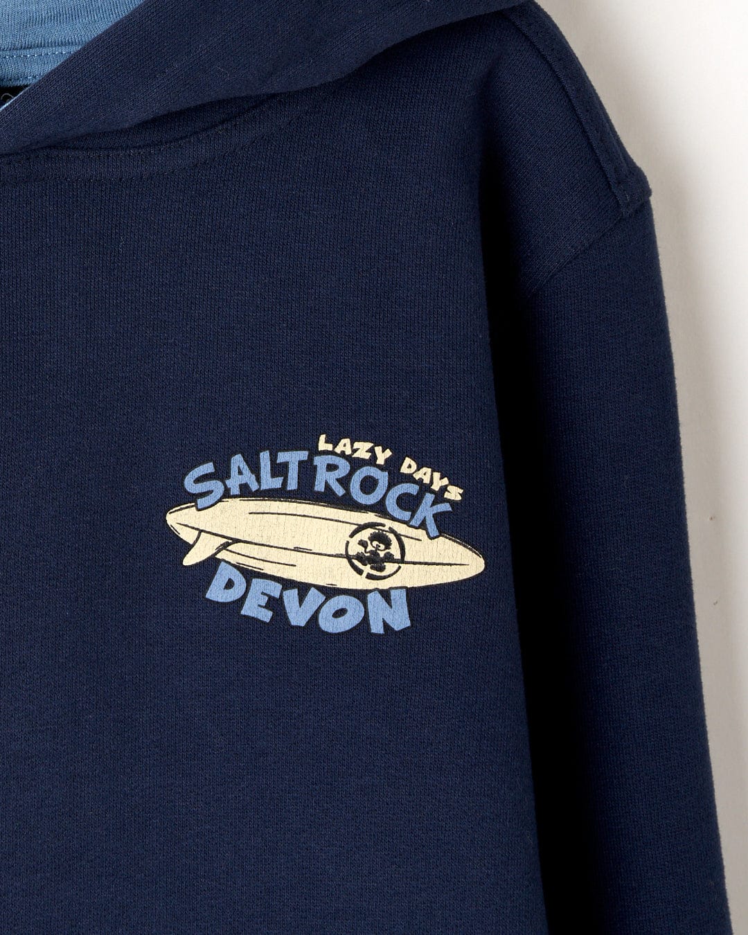Dark blue hoodie with the printed text "lazy day Saltrock Devon" and a surfboard graphic on its sleeve. (Lazy Location Devon - Recycled Kids Hoodie - Blue by Saltrock)