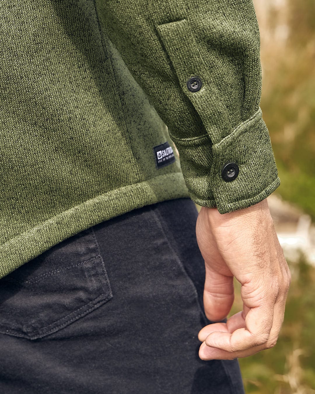 A stylish man wearing a green sweater, the Saltrock Levick - Mens Long Sleeve Shirt, and jeans.