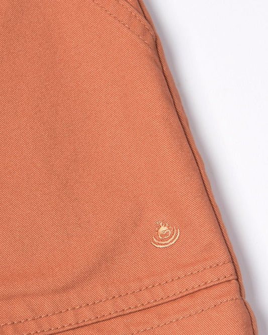 Close-up of Saltrock's Liesl Womens Chino Shorts - Brown, a terracotta-colored 100% cotton twill fabric with a small frayed hole.