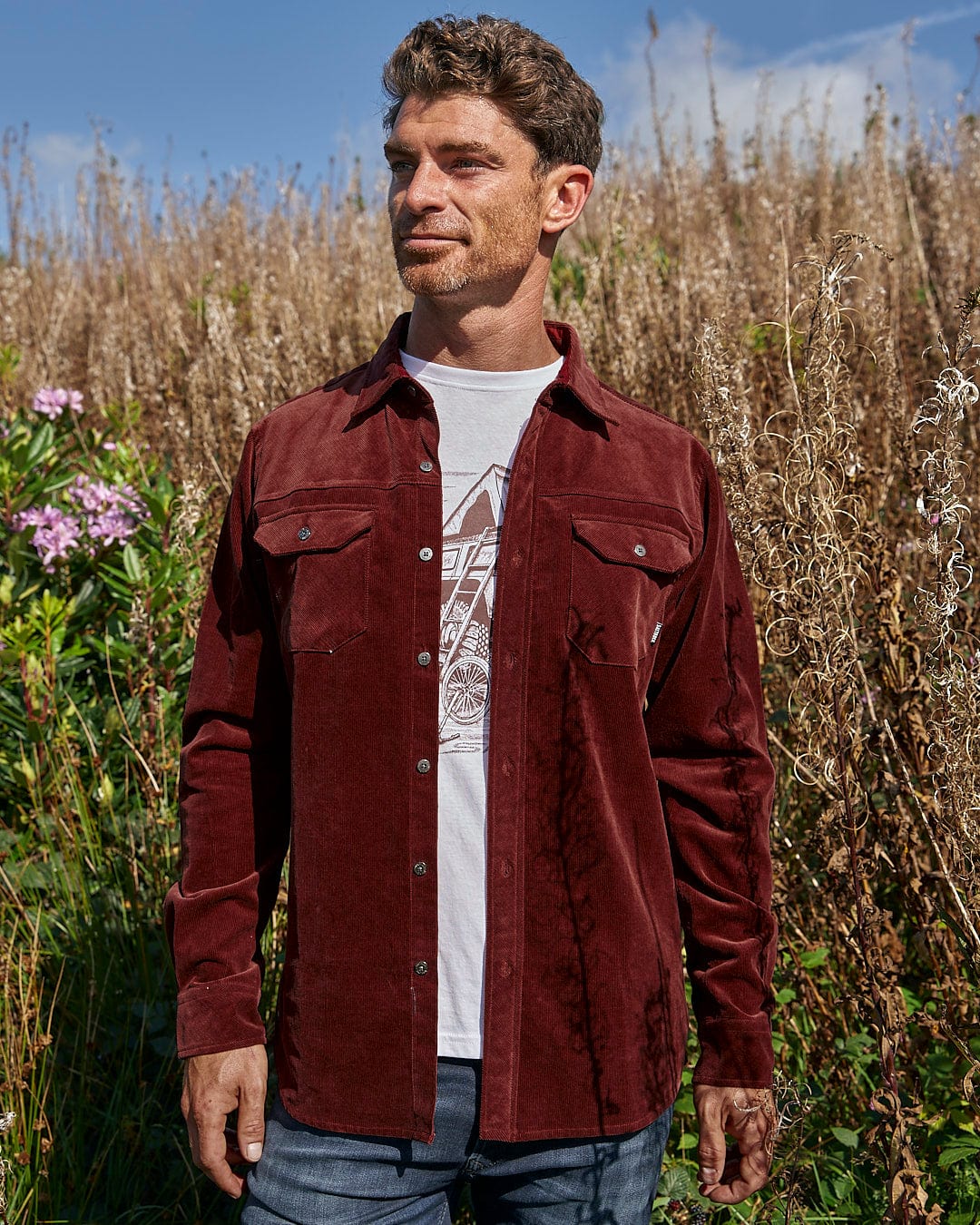 A man standing in a field wearing a Saltrock Linus - Mens Long Sleeve Shirt - Dark Red.