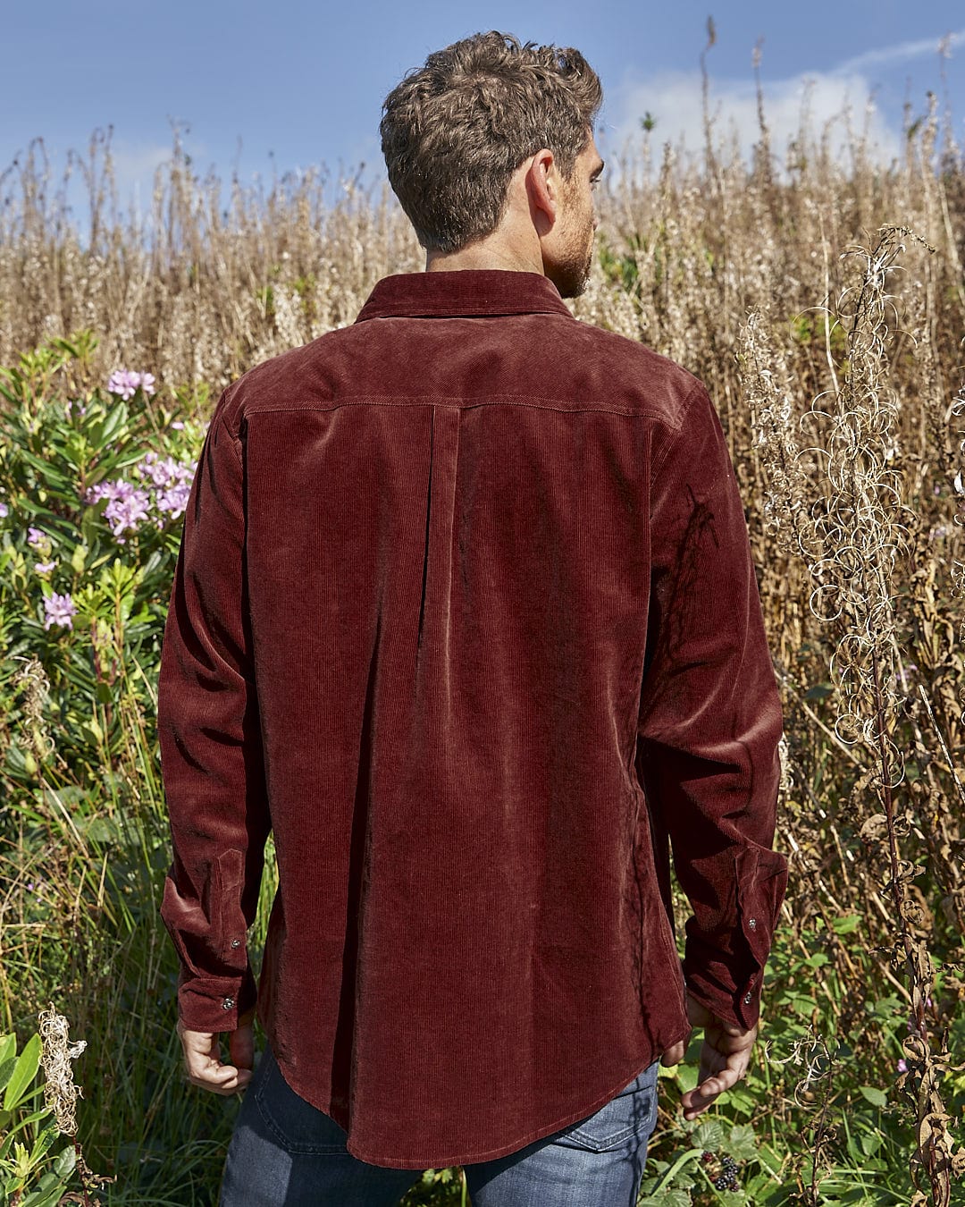 A man is standing in a field wearing a Saltrock Linus - Mens Long Sleeve Shirt - Dark Red.
