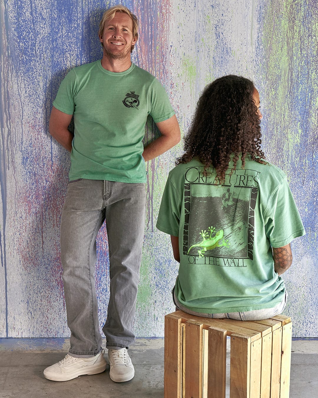 A man and woman are sitting on a stool next to a green wall wearing Little Creatures - Limited Edition 35 Years T-Shirt by Saltrock.