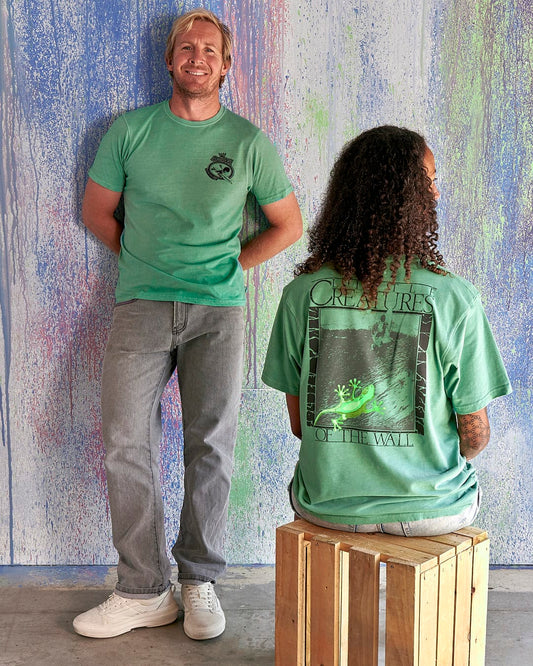 A man and woman are sitting on a stool next to a green wall wearing Little Creatures - Limited Edition 35 Years T-Shirt by Saltrock.