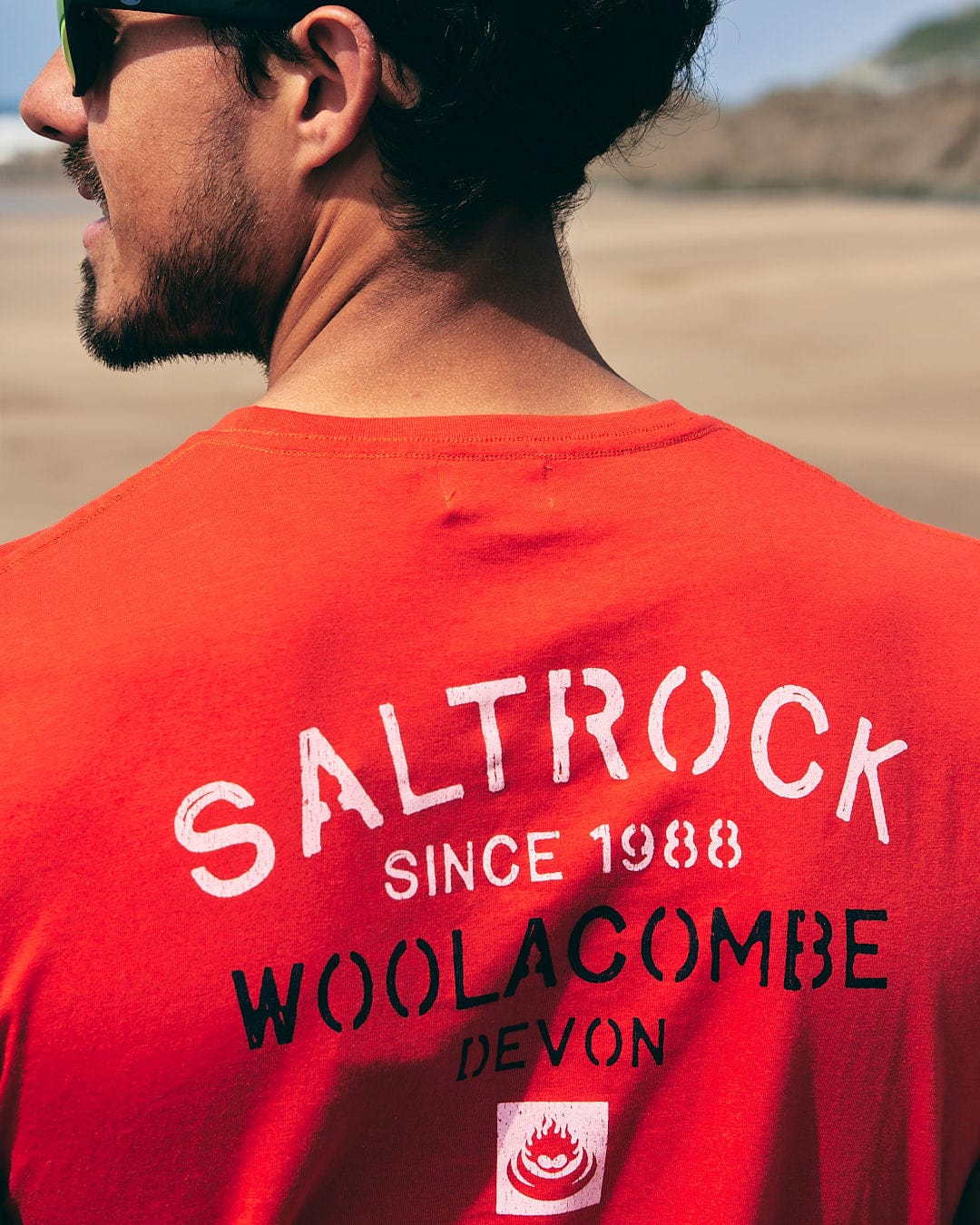 A man wearing a red t-shirt that says Saltrock Woolacombe Wool Devon.