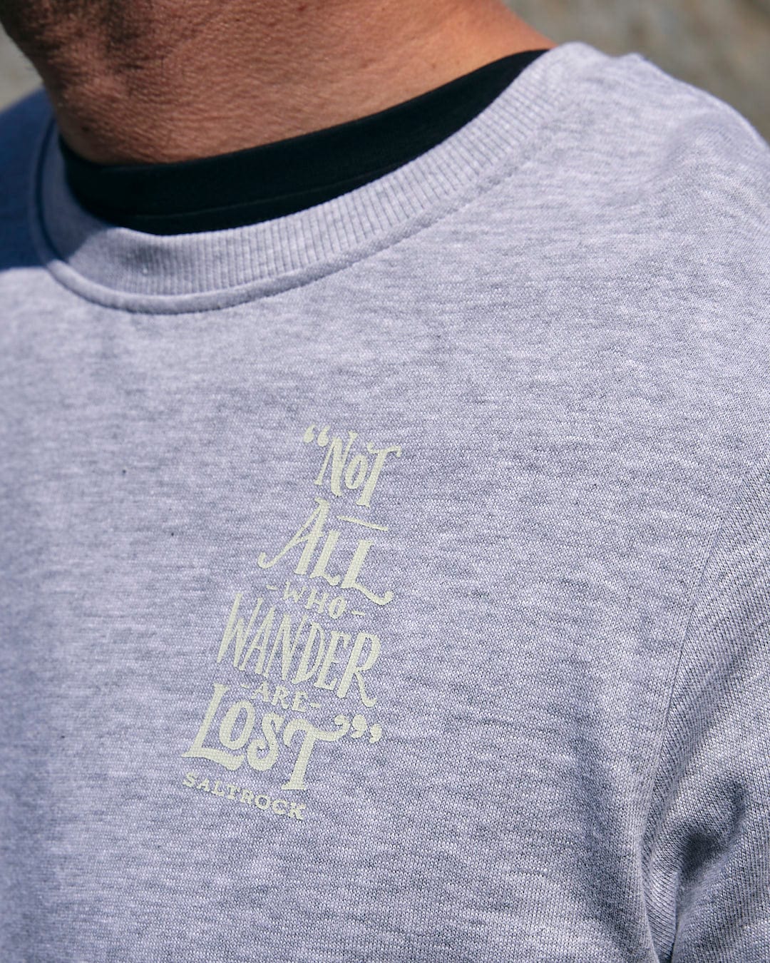 A man wearing a Saltrock Lost Ships - Mens Crew Sweat - Grey sweatshirt that says not all wander lost.