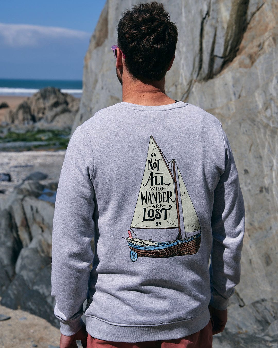 The back of a man wearing a Saltrock sweatshirt with the Lost Ships - Mens Crew Sweat - Grey sailboat on it.